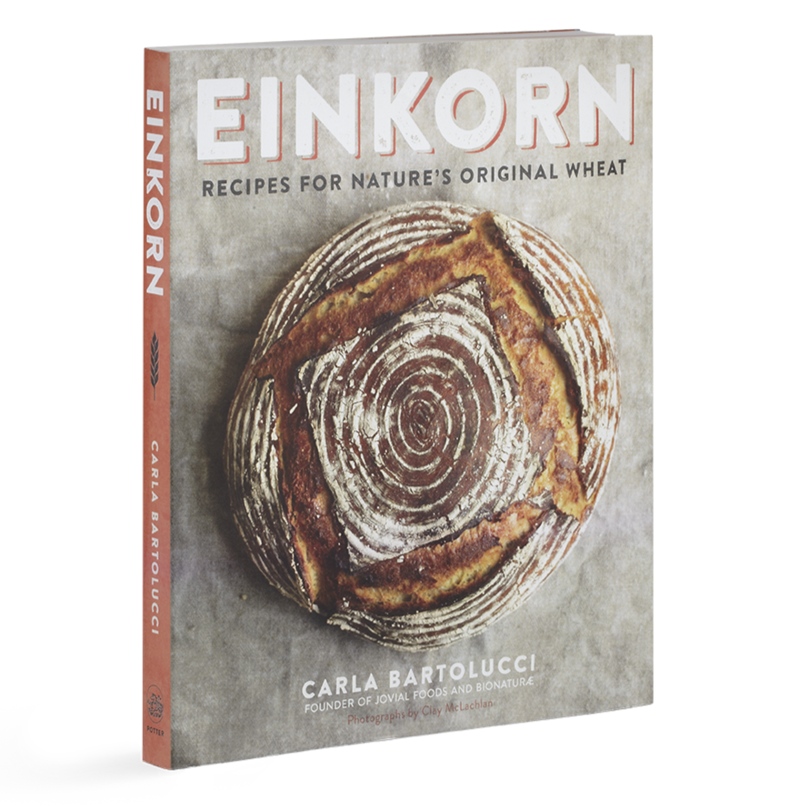 Three-quarter view of Einkorn cookbook showing front cover with title and round artisan loaf on a gray background