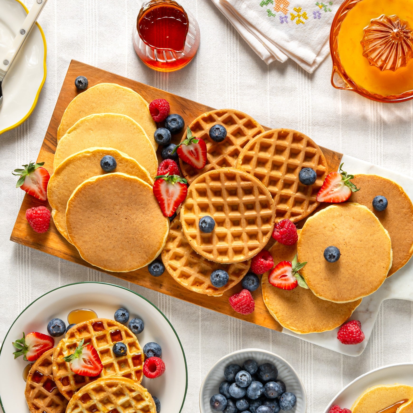 Einkorn pancakes and a heart-shaped waffle topped with fresh berries and maple syrup on a wooden serving board