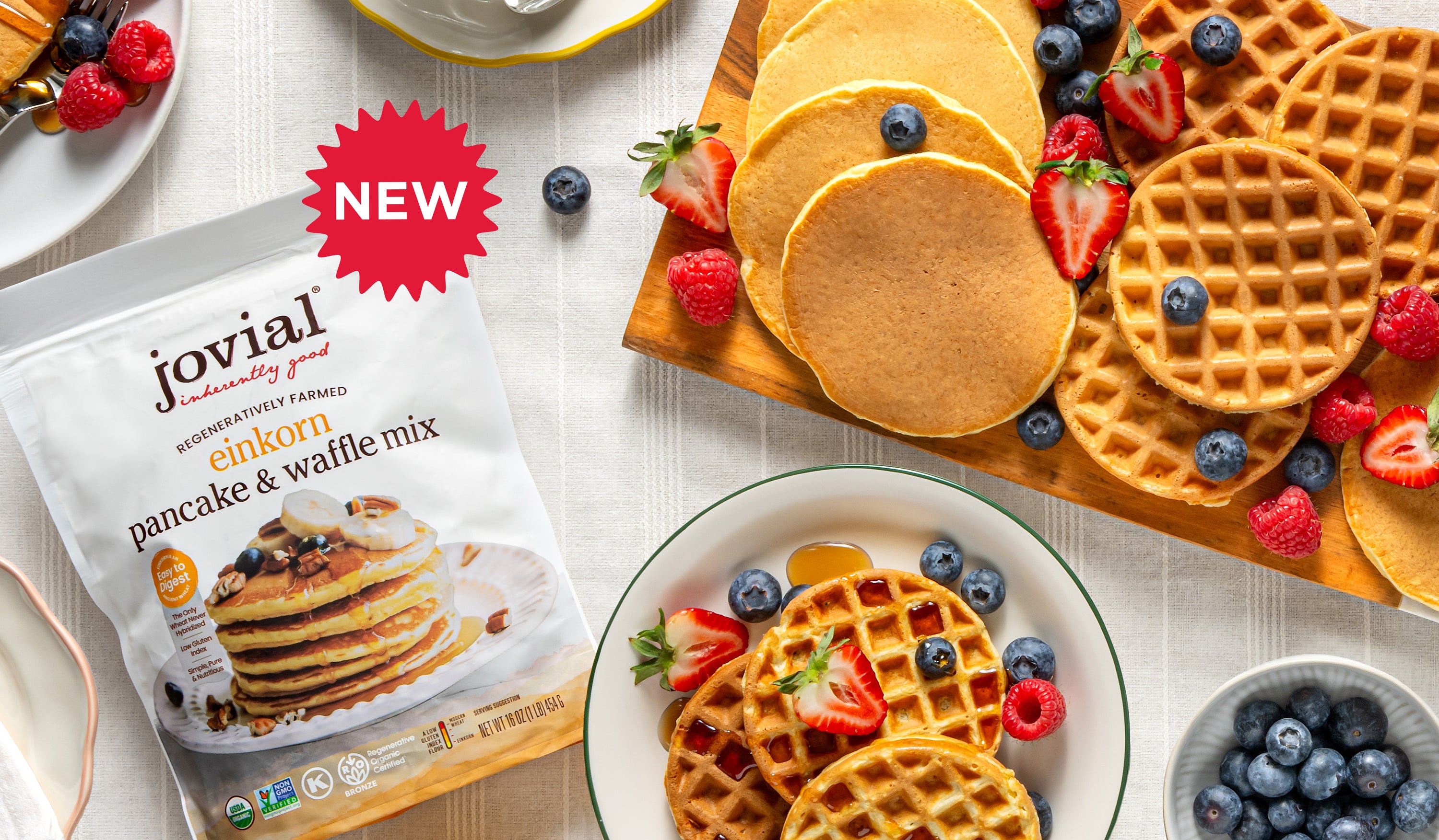 Angled view of Jovial Einkorn pancake & waffle mix bag showing NEW badge with plated pancakes and waffles topped with berries