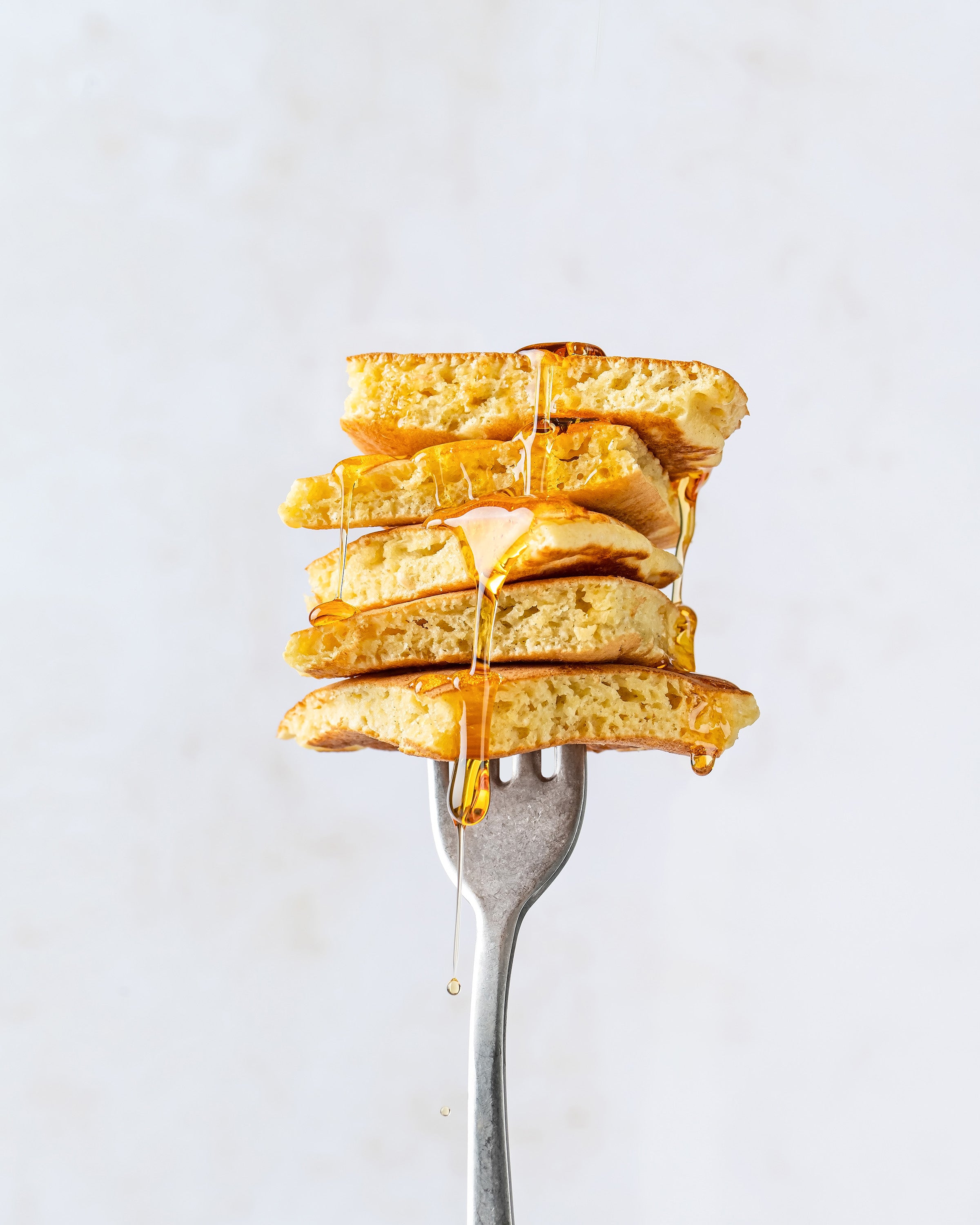 Stack of golden organic Einkorn pancakes on a fork with maple syrup dripping against a light neutral background