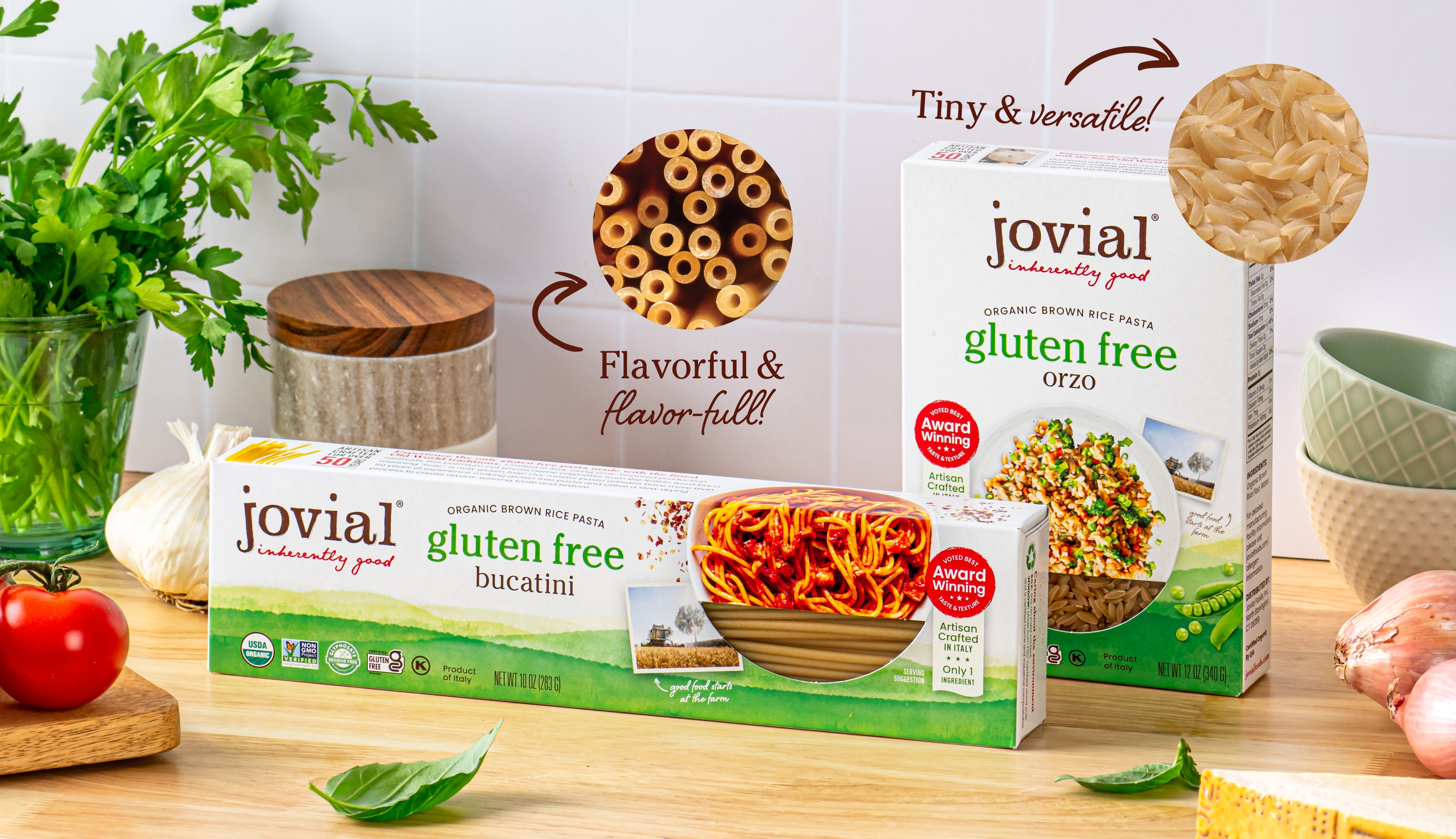 Front view of Jovial gluten free brown rice bucatini and orzo boxes showing packaging windows and pasta on a kitchen counter