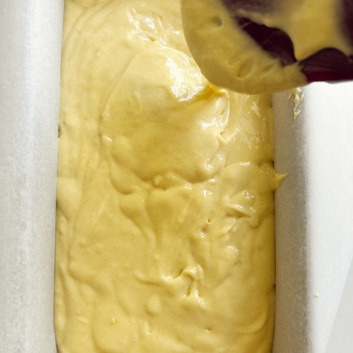 Einkorn lemon yogurt loaf batter being poured into a parchment-lined loaf pan