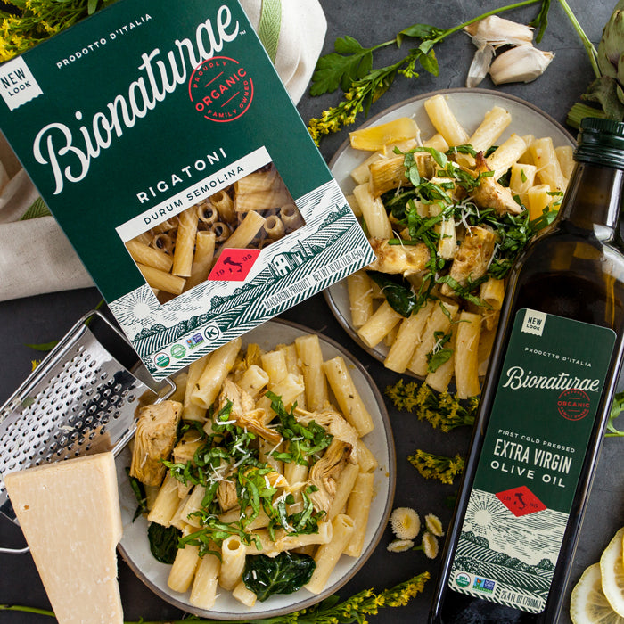 Two bowls of lemon basil rigatoni with roasted artichokes beside Bionaturae rigatoni and a bottle of extra virgin olive oil