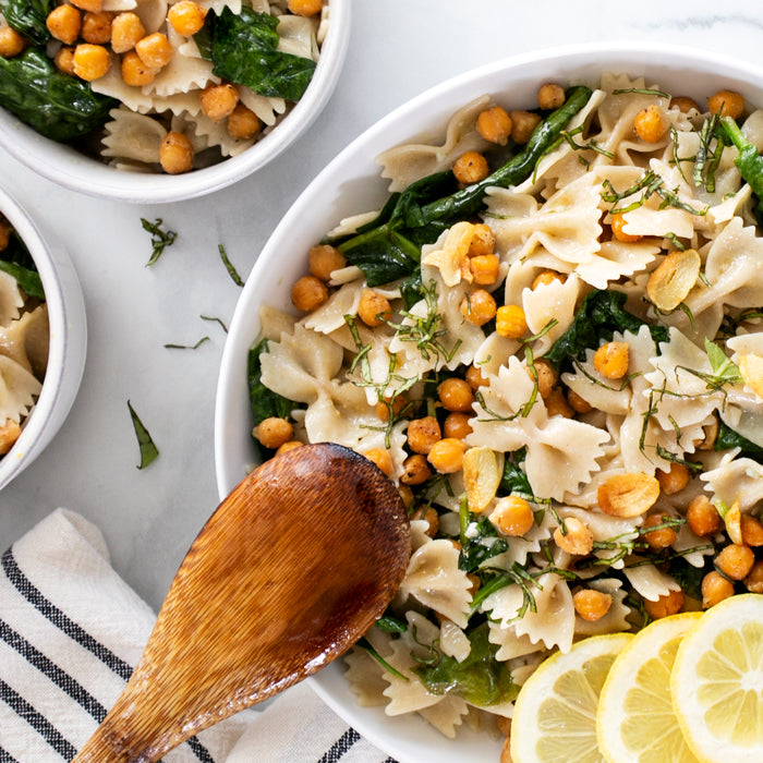 Bowl of lemon spinach farfalle with sauteed spinach, crispy chickpeas, garlic slices and lemon wedges