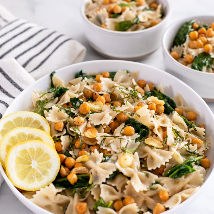 Overhead of lemon spinach farfalle with crispy chickpeas and lemon slices showcasing gluten-free brown rice pasta in a white bowl