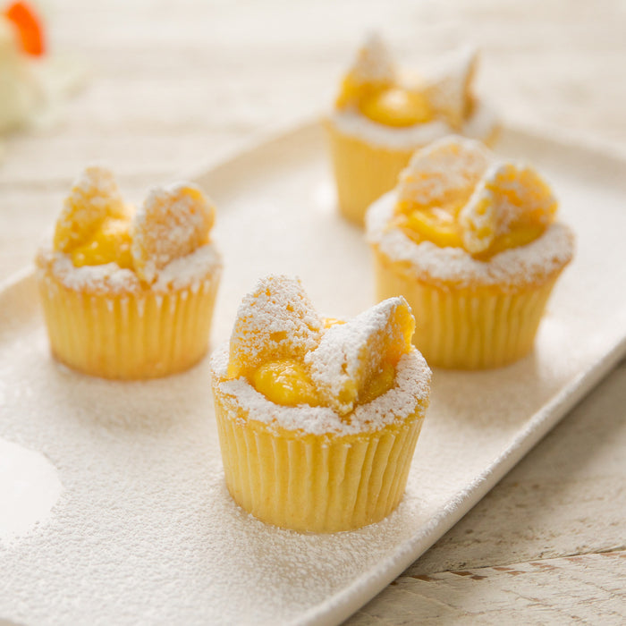 Close-up of Einkorn lemon cupcakes with lemon curd centers, powdered sugar, and paper liners on a white tray