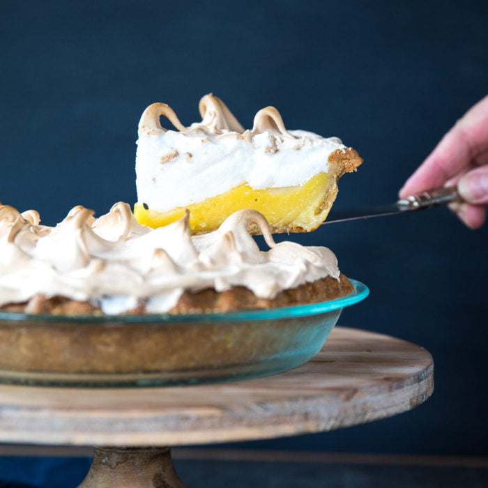 Side view of lemon meringue pie slice lifted from whole pie showing lemon curd and toasted meringue on Einkorn crust
