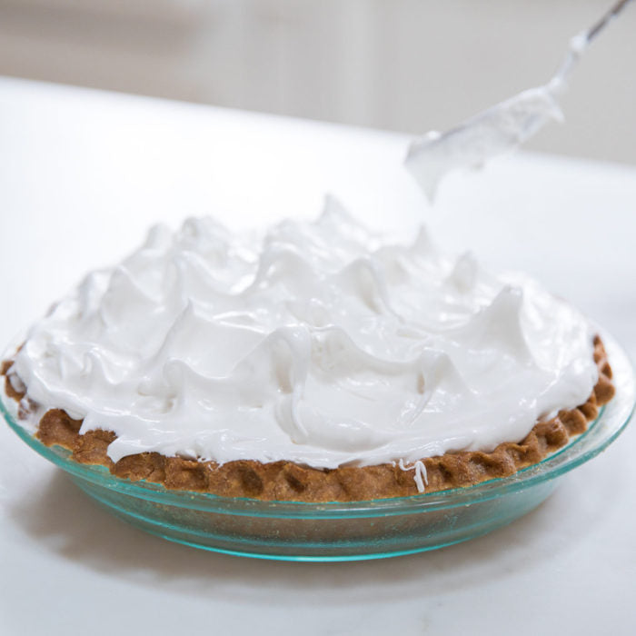 Side view of lemon meringue pie with glossy meringue peaks showcasing golden einkorn pie crust on a white countertop
