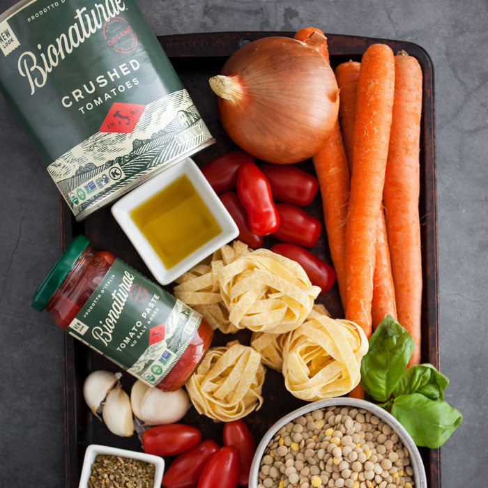 Tray of ingredients for lentil bolognese: Bionaturae crushed tomatoes, carrots, onion, garlic, pasta, lentils