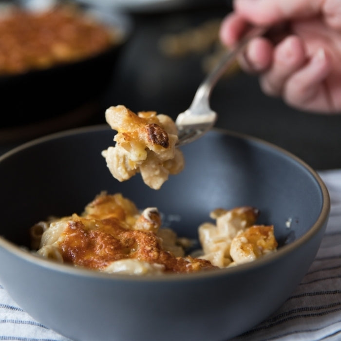 Baked mac and cheese with golden-brown crust in a gray bowl, fork lifting a cheesy serving