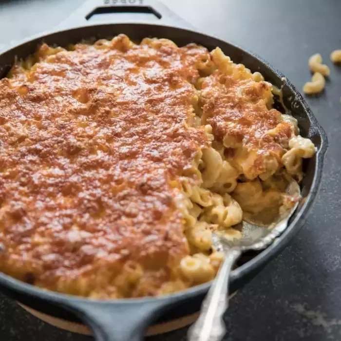 Baked macaroni and cheese in a cast-iron skillet with a golden, crispy cheese crust and a spoon serving a portion