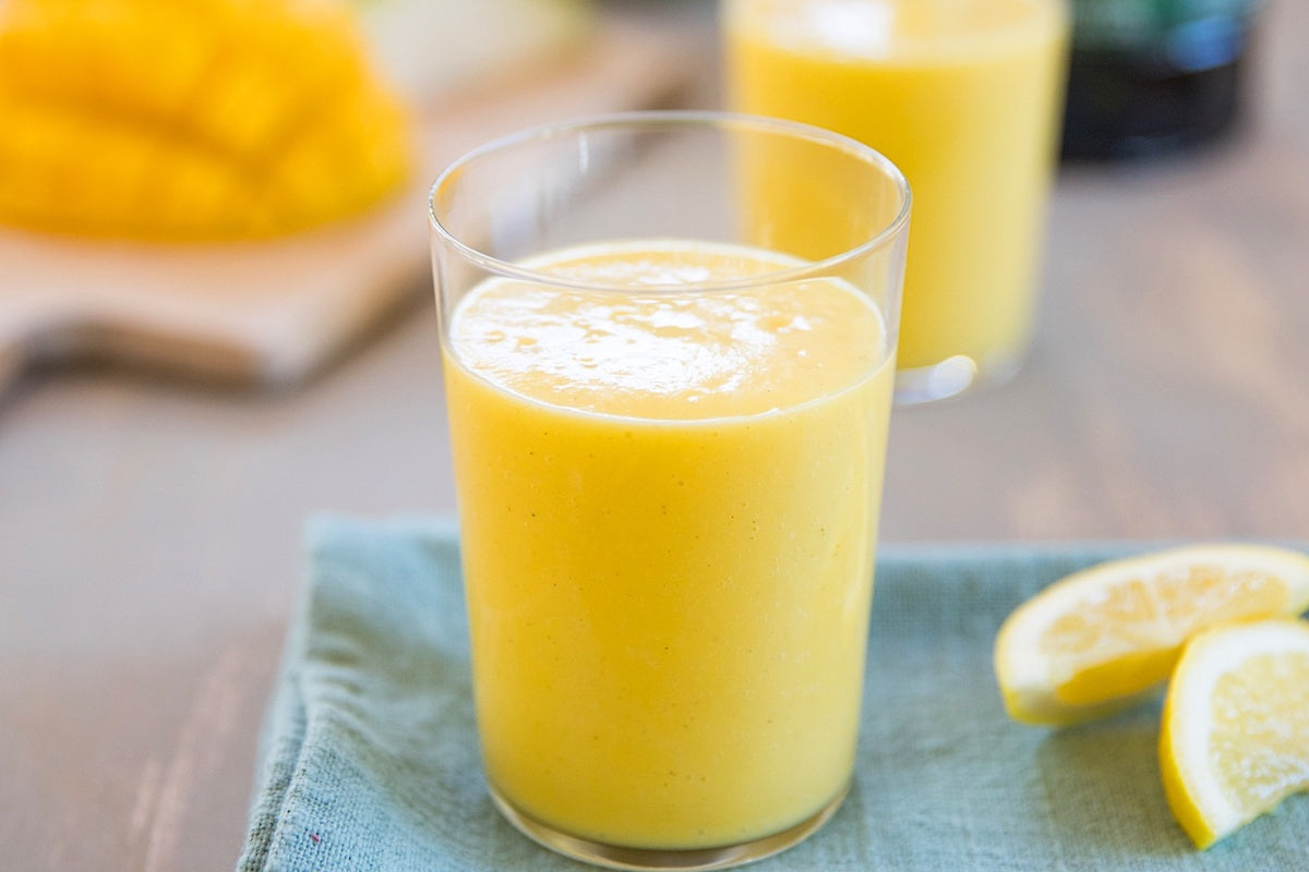 Glass of pear-mango smoothie with creamy texture on a blue napkin, lemon wedges and blurred second glass