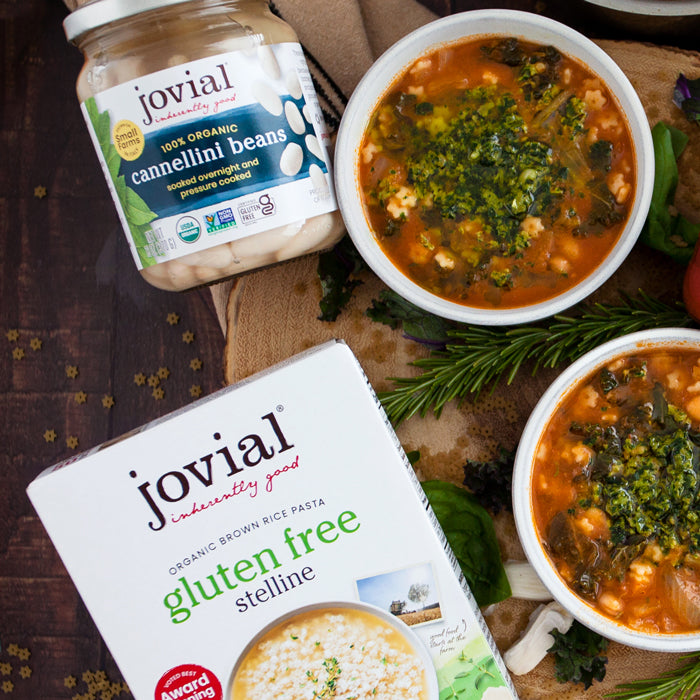 Two bowls of rosemary minestrone topped with spinach pesto beside Jovial gluten free stelline pasta box and jar of cannellini beans