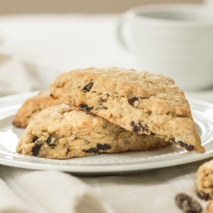 Close-up of two triangular Einkorn Morning Glory scones stacked on a white plate showing crumbly texture and raisins with a soft neutral background
