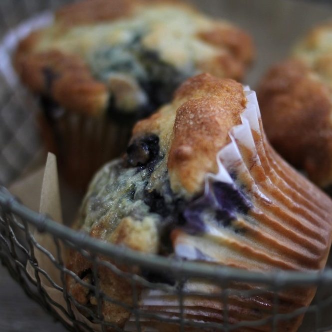 Close-up of an Einkorn blueberry muffin showing a golden domed top and visible blueberries in a wire basket