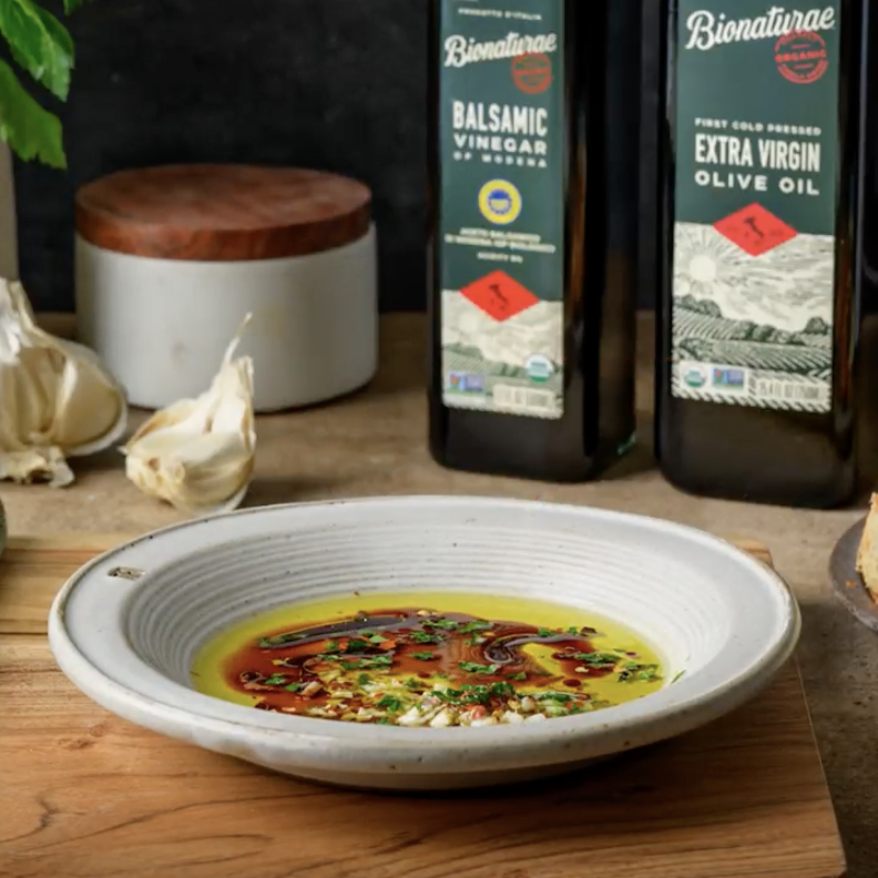 Two Bionaturae organic balsamic vinegar bottles beside a bowl of vinaigrette on a wooden counter