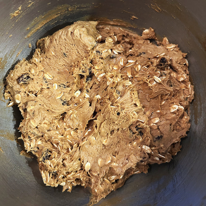 Sourdough einkorn oatmeal raisin cookie dough resting in a metal mixing bowl with visible oats and raisins
