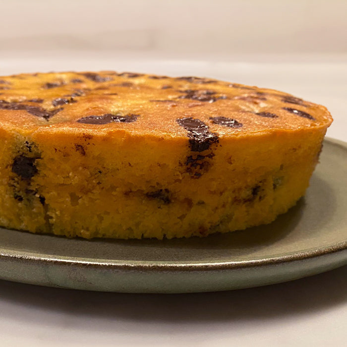 Close-up side view of einkorn ricotta cake with chocolate chips and golden crumb on a stoneware plate