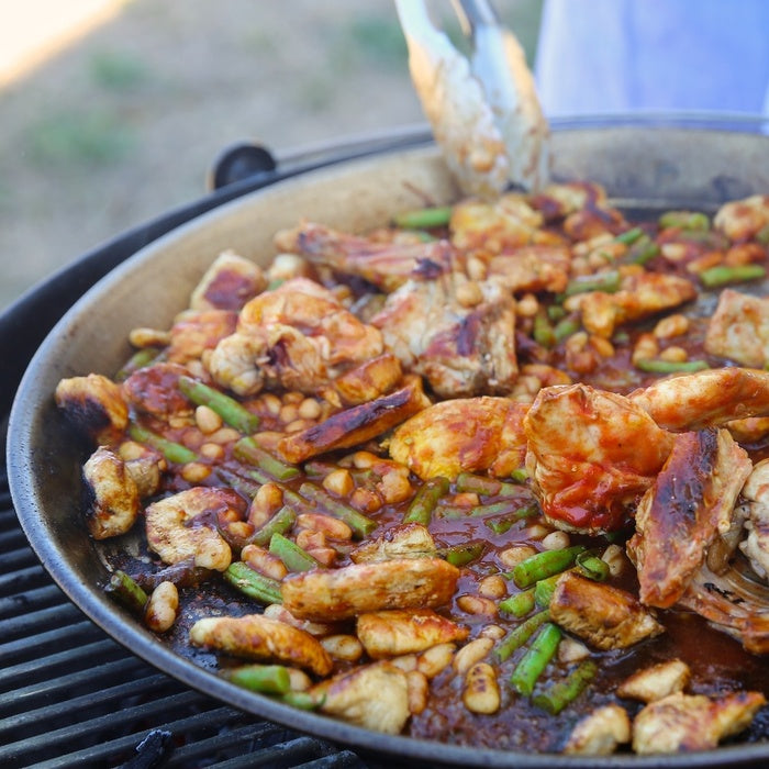 Paella with chicken, shrimp, green beans, and cannellini beans simmering in a paella pan on a grill