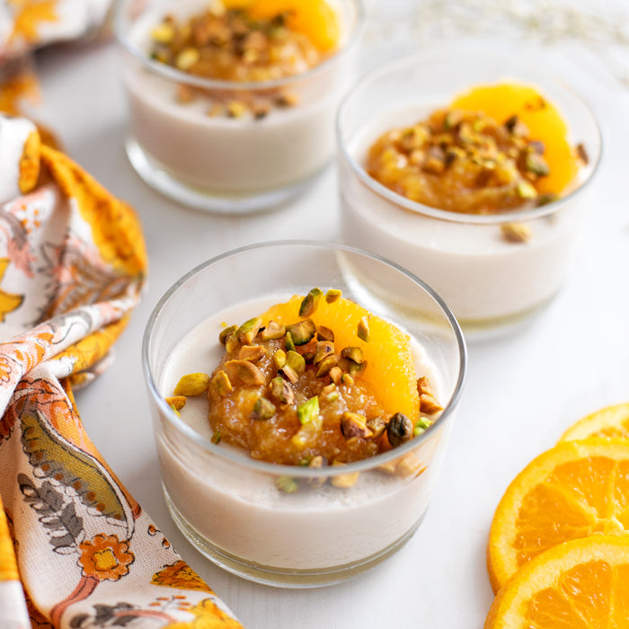 Panna cotta in glass cups topped with organic apricot compote and crushed pistachios, with orange slices