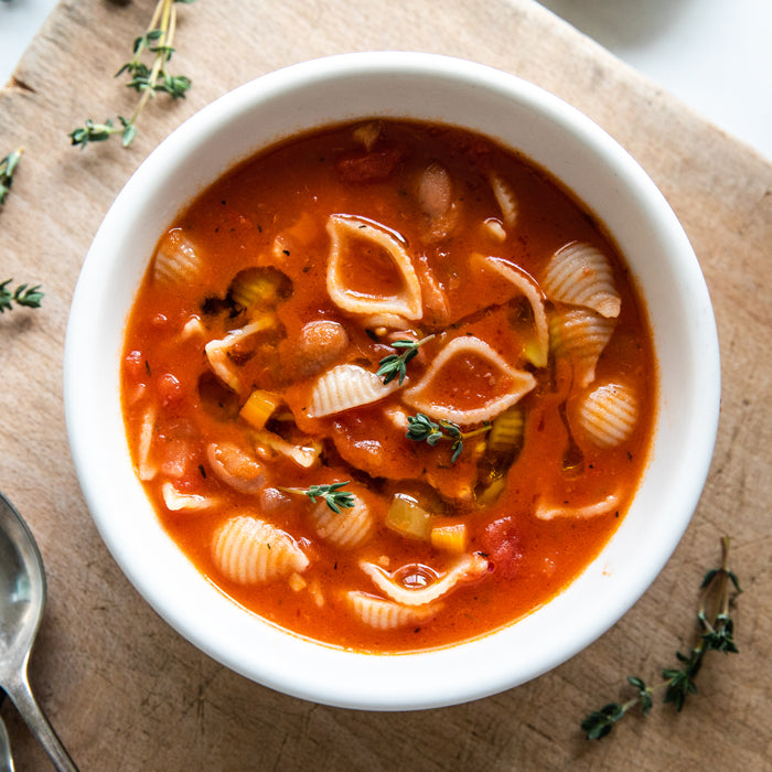 Bowl of traditional Italian pasta e fagioli with shell pasta and beans, garnished with thyme on a wooden board