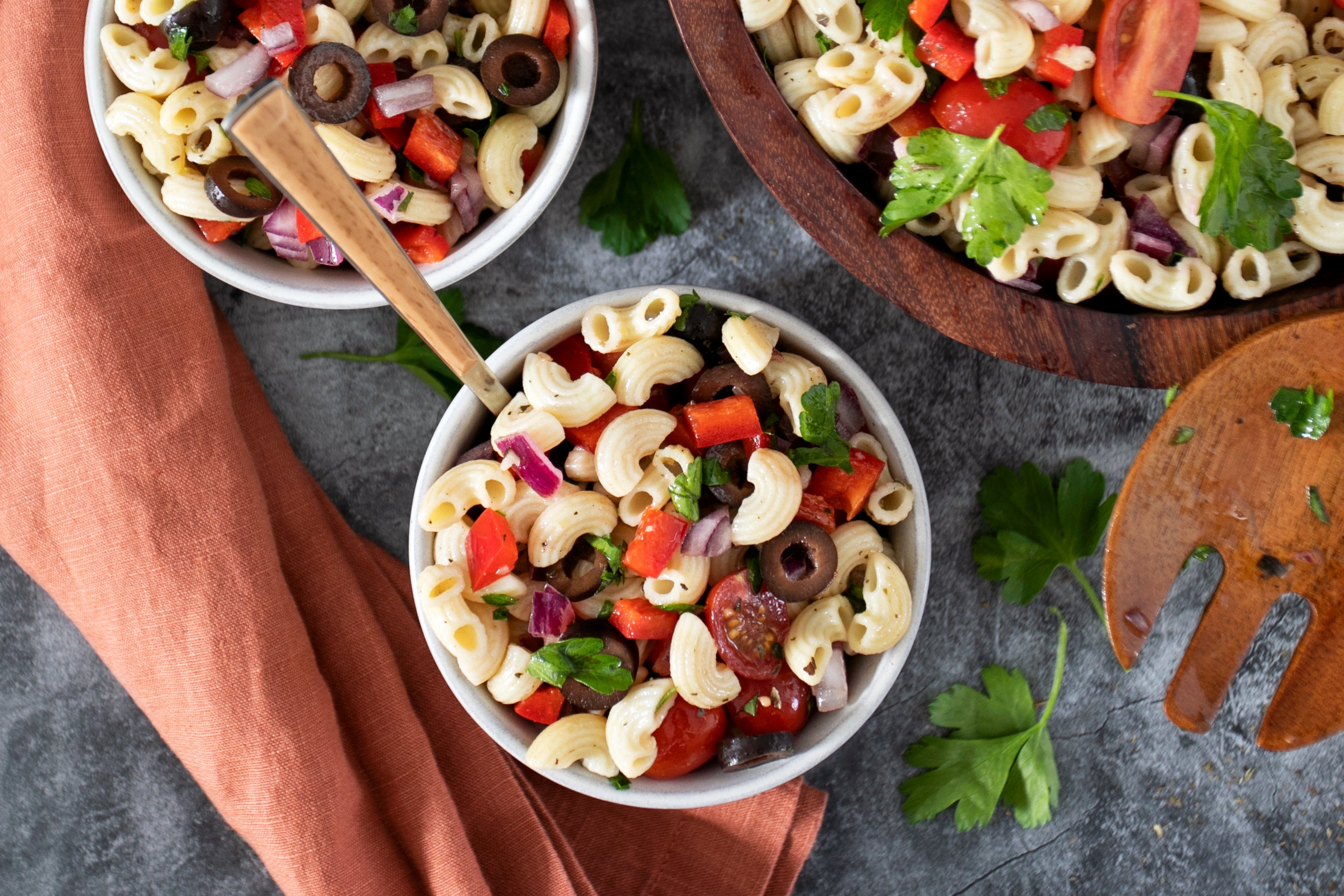 Bowls of pasta salad made with gluten-free elbow pasta, cherry tomatoes, olives, red pepper, red onion, and parsley