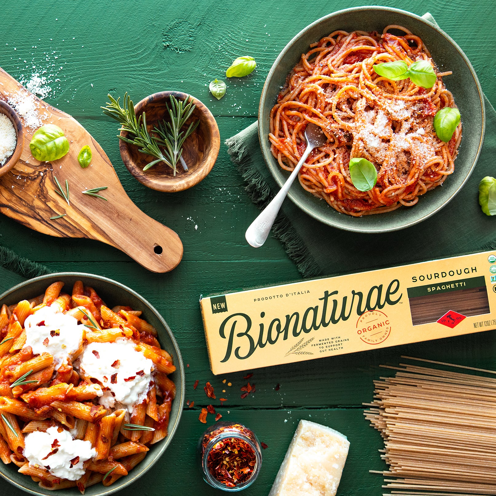 Bionaturae sourdough spaghetti box beside bowls of pasta in tomato sauce with basil and grated cheese on a green table