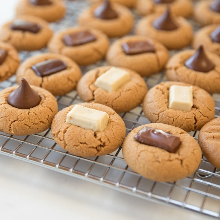 Close-up of Einkorn peanut butter blossom cookies on a wire cooling rack, each topped with a chocolate kiss or a chocolate square