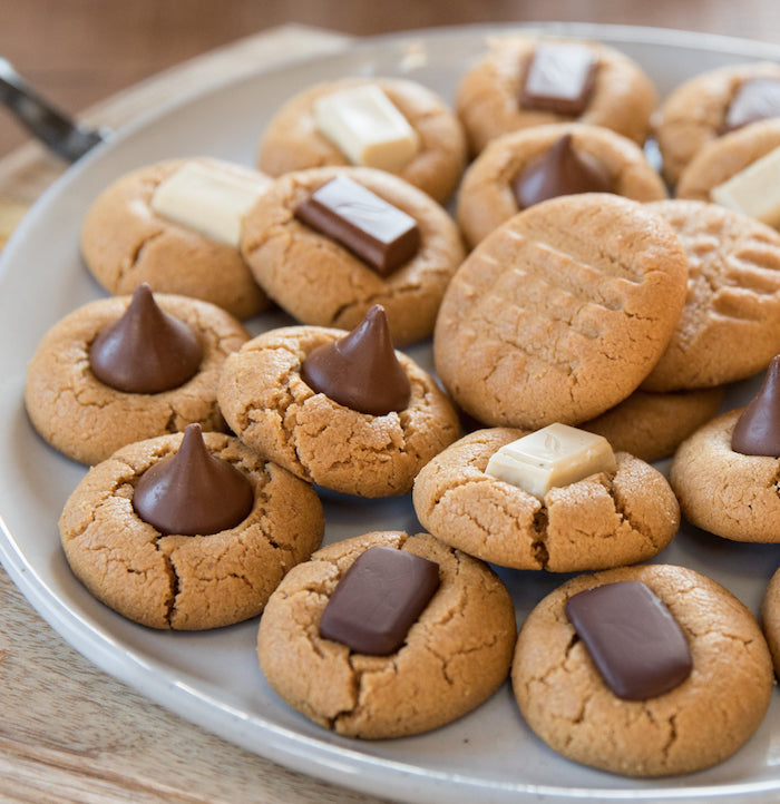 Overhead of Einkorn peanut butter blossom cookies with cracked centers topped with assorted chocolate pieces on a gray plate