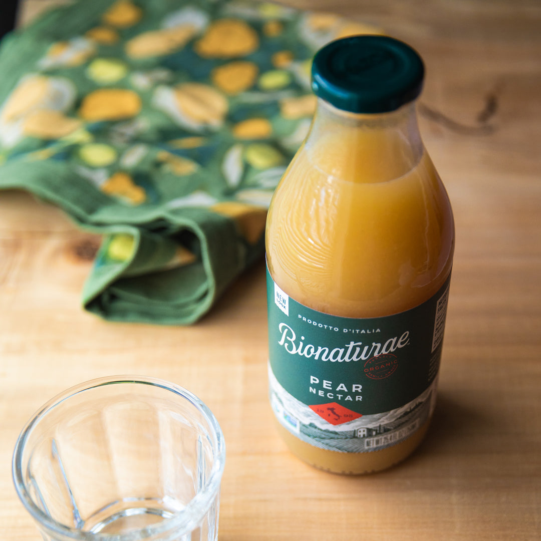 Three-quarter view of Organic Pear Nectar 25.4 oz bottle showing glass packaging on a wooden table
