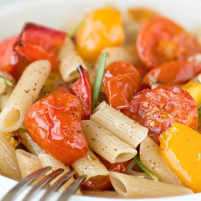 Close-up of Einkorn penne tossed with oven-roasted cherry tomatoes and yellow peppers, garnished with rosemary on a white plate