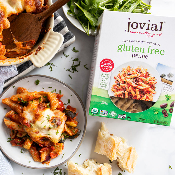 Vegetable penne pasta bake on a plate beside a Jovial gluten free penne box with torn bread