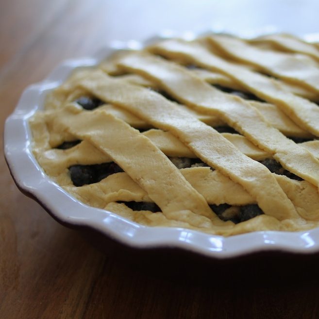 Close-up of blueberry pie with lattice top crust in a white ceramic pie dish on a wooden table