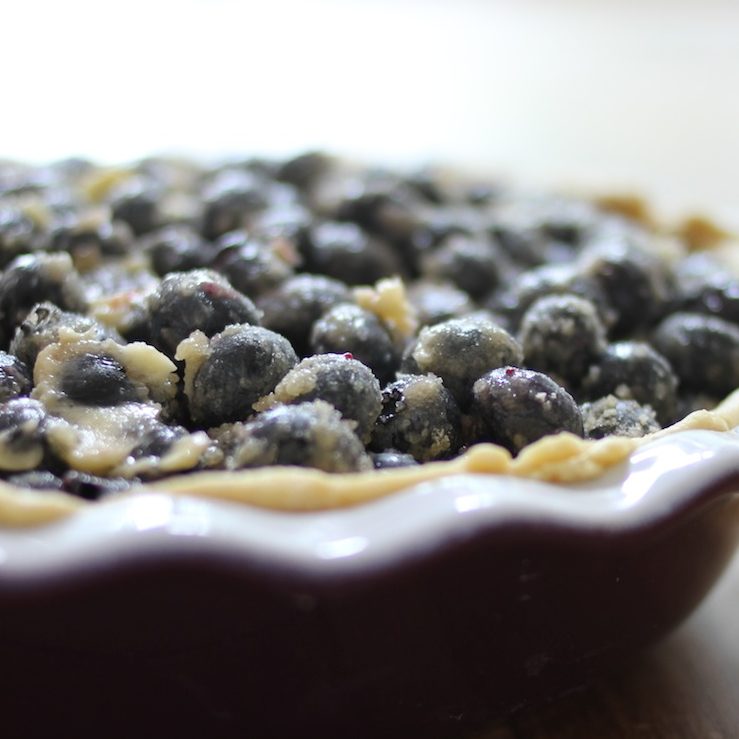 Close-up of lighter blueberry pie showing juicy sugared blueberries and flaky golden einkorn crust in a red ceramic pie dish