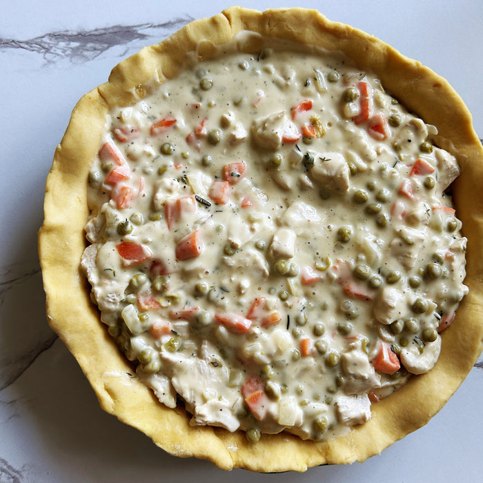 Top-down view of chicken pot pie with sourdough crust, creamy filling of chicken, peas, and carrots on marble surface