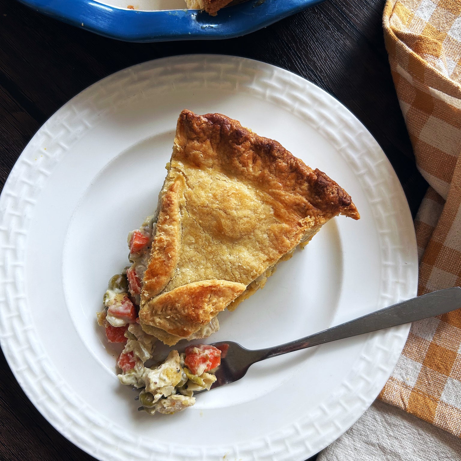 Top-down view of a slice of sourdough chicken pot pie with flaky golden crust and carrots and peas on a white plate