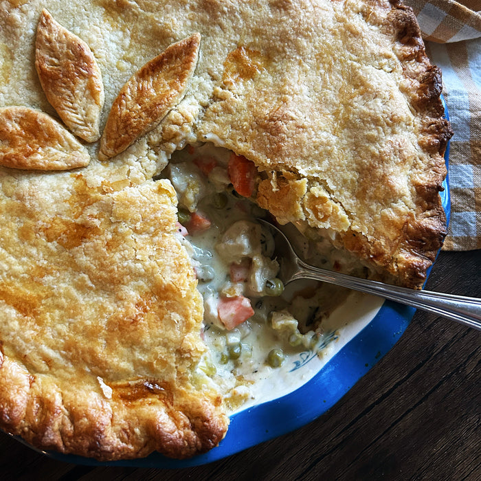 Overhead close-up of sourdough chicken pot pie with a slice removed, showing creamy chicken, peas, and carrots in a blue dish