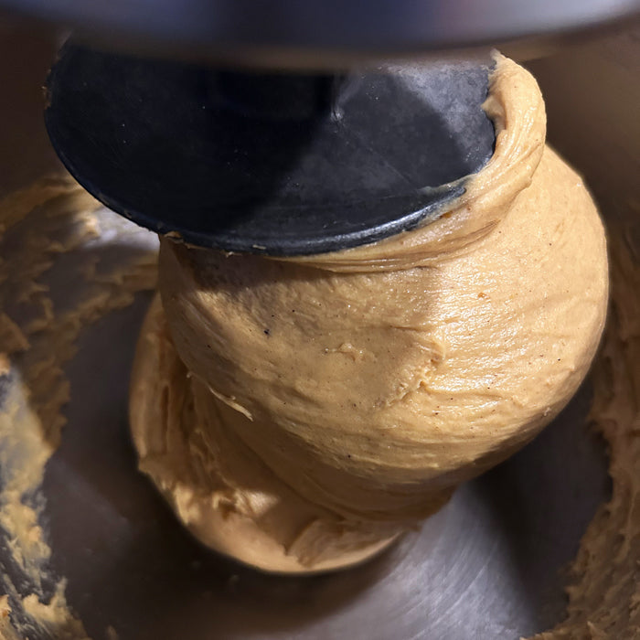 Pumpkin einkorn donut dough being mixed in a stand mixer bowl, showing smooth orange-brown dough texture
