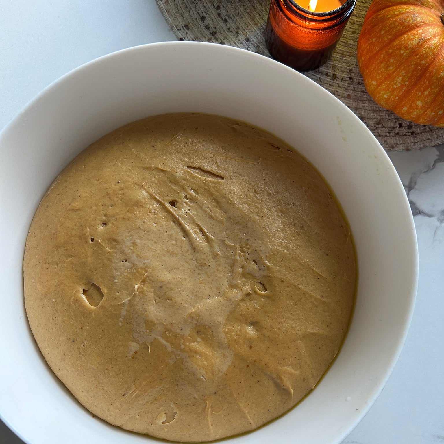 Top-down view of a bowl of risen pumpkin einkorn sourdough donut dough showing a smooth, spongy surface in a white mixing bowl