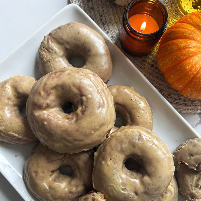 Angled view of sourdough pumpkin einkorn donuts on white plate showcasing brown butter maple glaze with pumpkin and candle