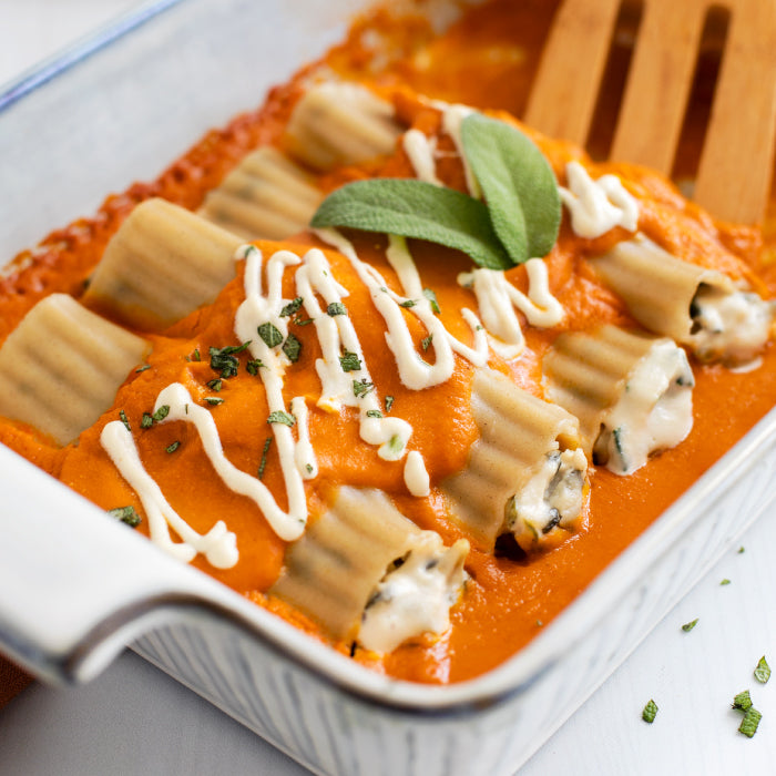 Manicotti in pumpkin-sage sauce, stuffed with cashew ricotta and spinach, topped with fresh sage and white sauce drizzle