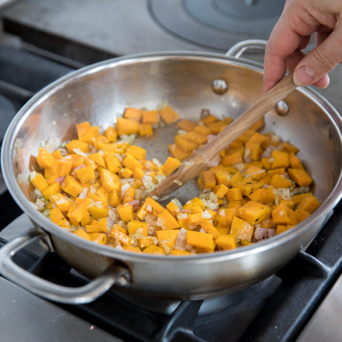 Hand stirring diced squash, onion, and pancetta in a stainless-steel skillet to make croquette filling