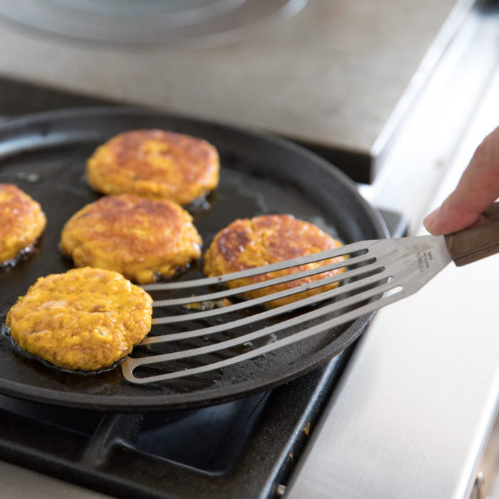 Einkorn squash croquettes frying in a cast-iron skillet on a stovetop as a spatula lifts one