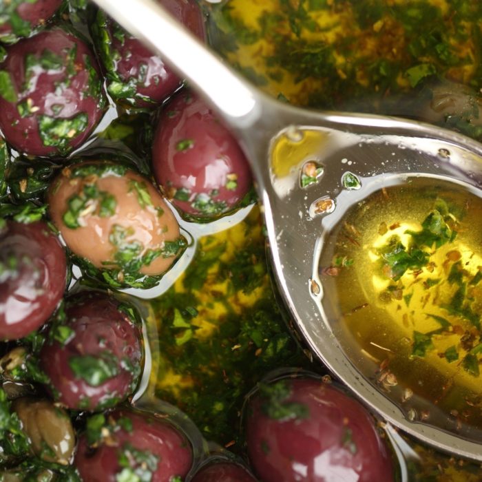 Close-up of marinated olives in olive oil with chopped basil and a metal spoon