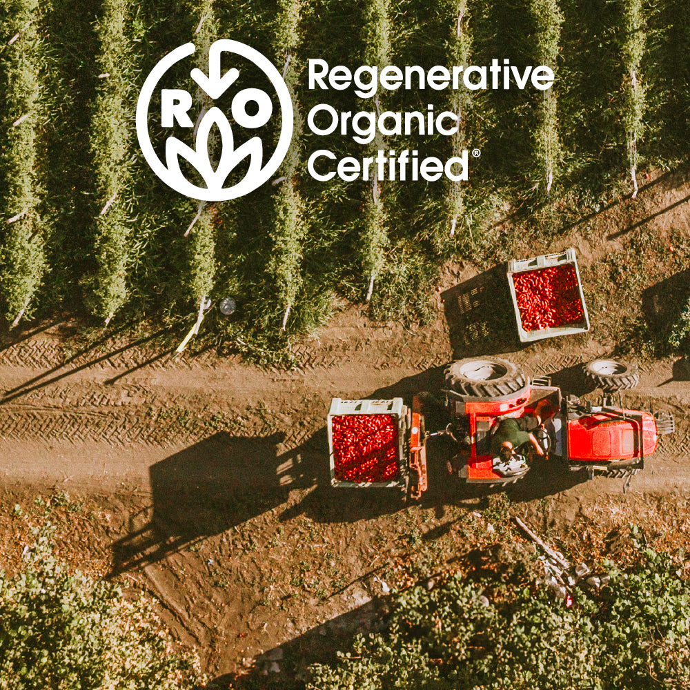 Aerial view of a tractor hauling crates of harvested red tomatoes through crop rows with ‘Regenerative Organic Certified’ logo overlay