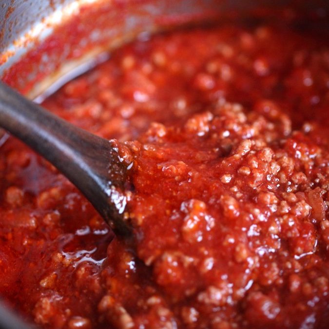 Gluten-free Bolognese sauce simmering in a pot with a wooden spoon, rich tomato and ground-meat texture