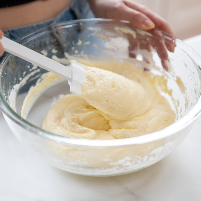 Einkorn ricotta cake batter being folded with a spatula in a glass bowl, ready for baking