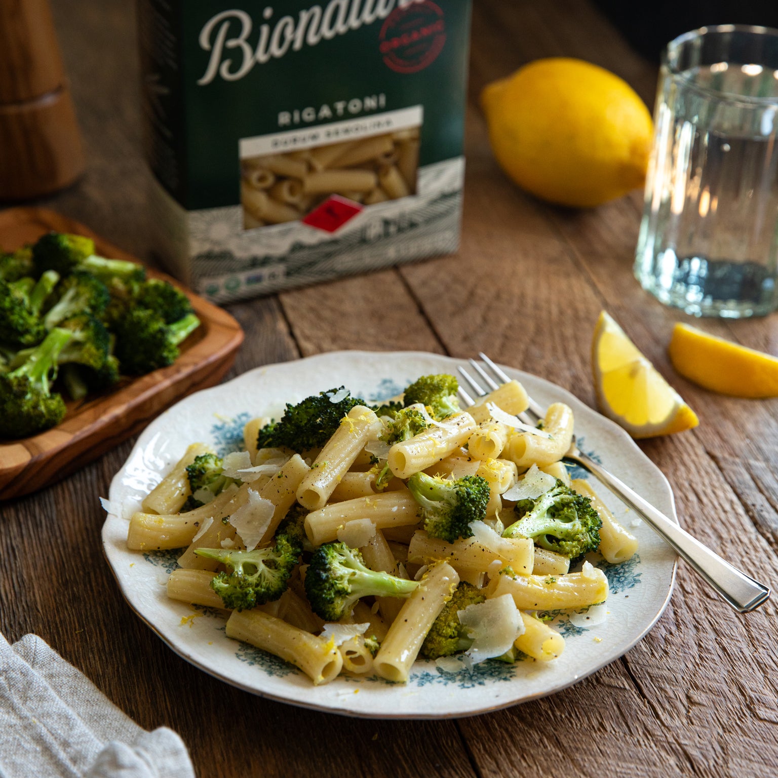 Plate of rigatoni with roasted broccoli and shaved cheese, Bionaturae rigatoni box and lemon wedge in the background