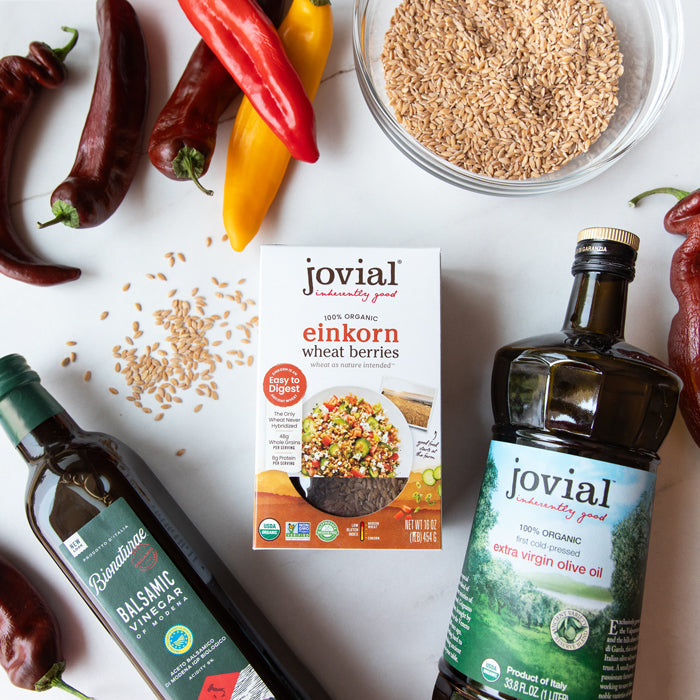 Top-down view of Jovial einkorn wheat berries box showing serving photo and ‘100% organic’ label, with olive oil, balsamic vinegar, roasted peppers, and a bowl of grains