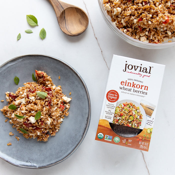 Roasted pepper einkorn wheat berry salad on gray plate beside Jovial organic Einkorn Wheat Berries box and wooden spoon